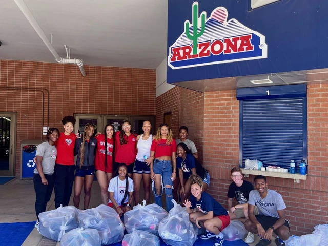 A group of students outside stand and kneel around plastic bags full of shoes