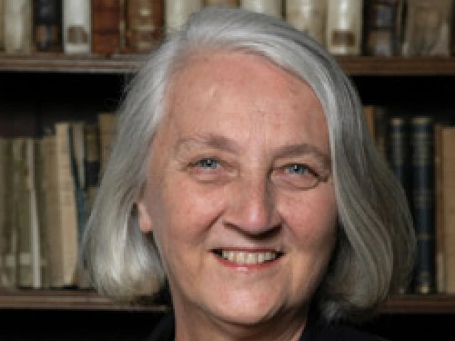 A woman with silver hair smiles in front of a bookshelf