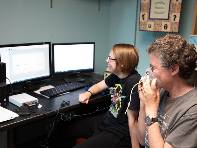 A professor and student sit in front of computer screens while using a breathing apparatus tool for research