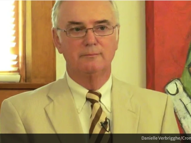 George Cunningham, in a cream colored suit and wearing glasses, stands in front of a brightly colored piece of art