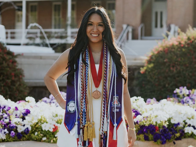 Student with long brown hair stands in front of Old Main, wearing graduation regalia