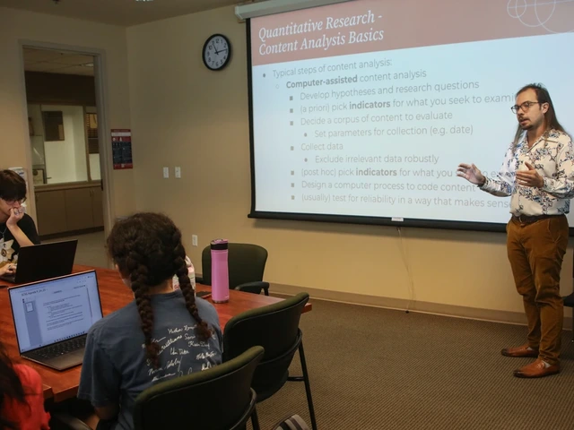 Man with long hair and glasses stands in front of a classroom and projection screen, teaching
