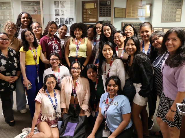 A group of young Latin American women scholars and NNI/UA staff posed together in front of a trophy case in a bright indoor space. They smile broadly, wearing casual clothing, as they celebrate their participation in the SUSI Women’s Leadership program