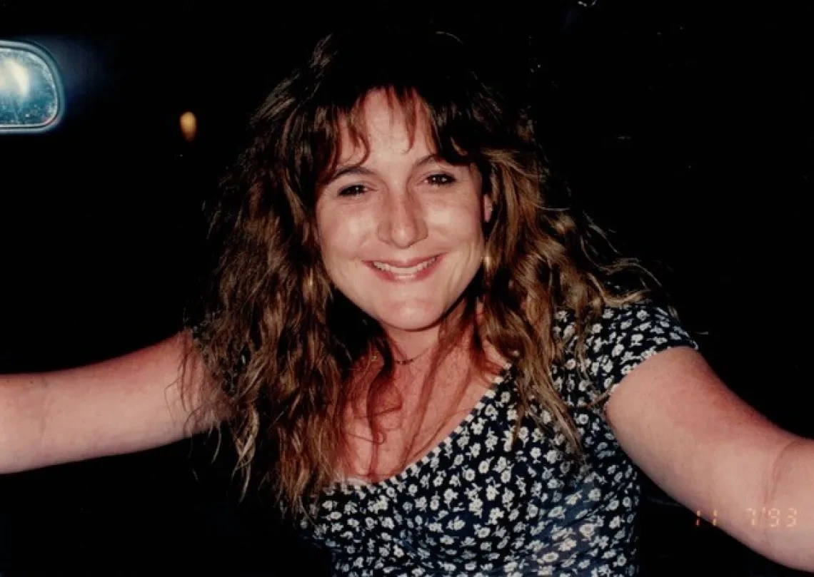 Woman with long curly hair and wearing a black and white flowered top smiles broadly