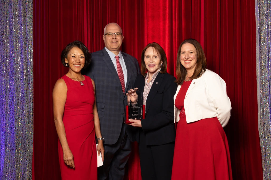 Three women and one man stand together for a photo in a formal setting