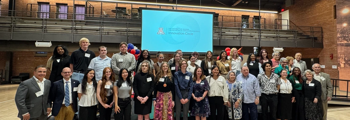 Large group of students, faculty and donors stand in a group in a gym, smiling for a photo