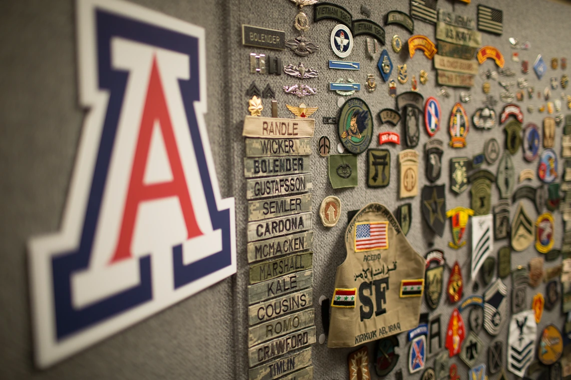 A wall with an "A" logo and also military-related pins, medals, badges and patched