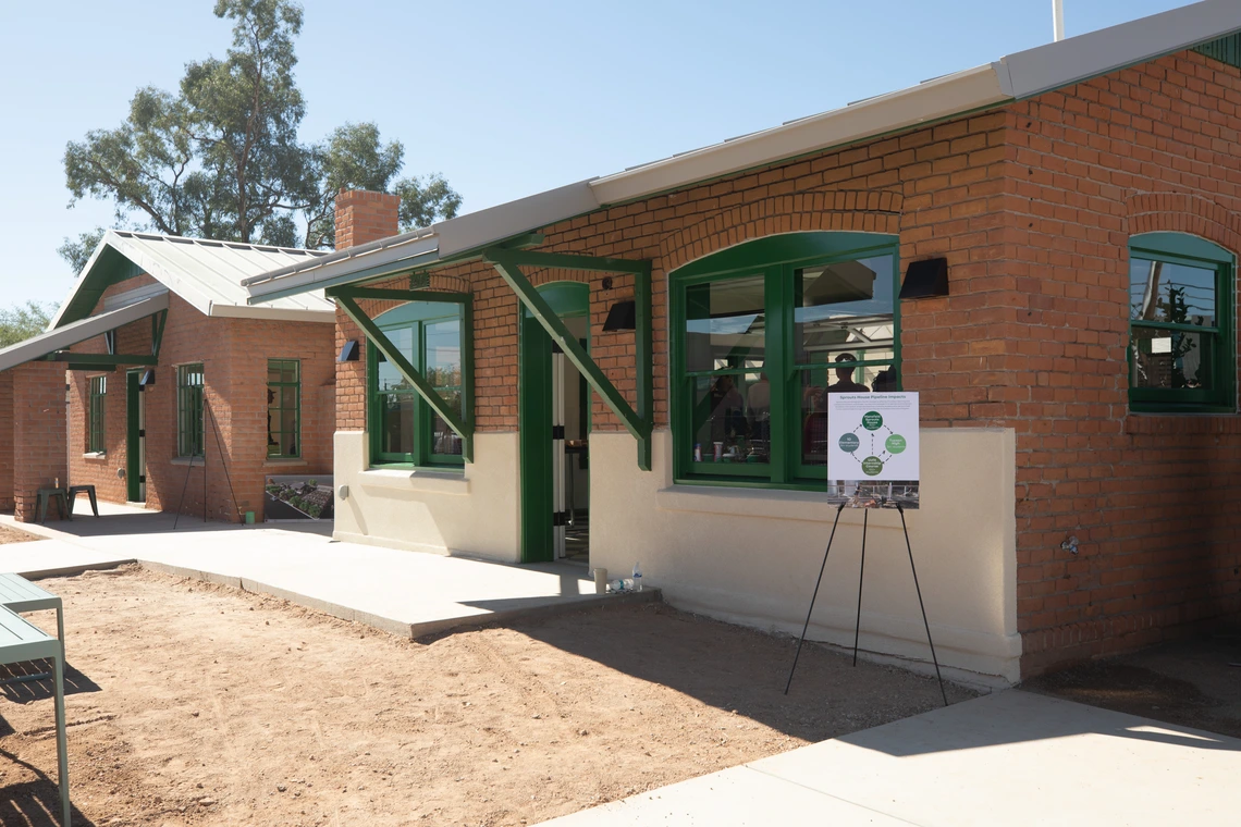 Two renovated brick homes with green trim. There is a sign on an easel and chair and benches set up for guests.