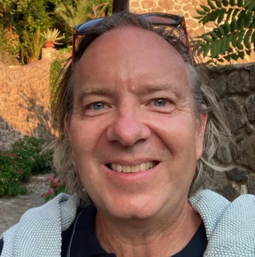 Brian Silverstein stands outside wearing sunglasses on his head and smiling