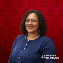 Woman with black hair and blue blouse sits in front of red background
