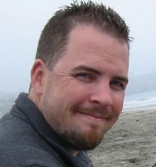Man with brown hair and goatee outside, smiling