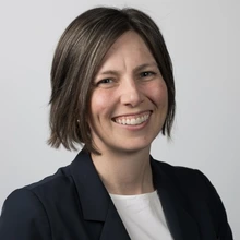 Woman with a short bob wearing a black jacket and white top smiles