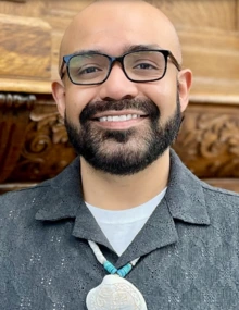 Man with glasses and dark beard wearing Indigenous jewelry