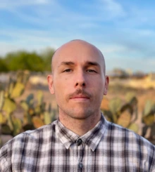 Man with mustache and wearing a plaid shirt standing in the desert