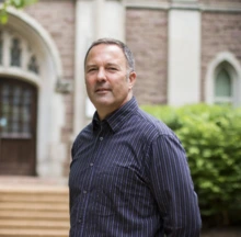 Man in a navy blue shirt stands in front of an old building