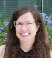 Woman with glasses sits outside in front of blue flowers
