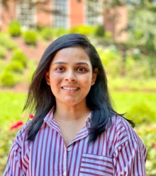 Woman with long brown hair and wearing a striped shirt stands outside