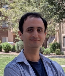 Man with black hair, wearing a blue shirt stands outside