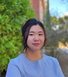 Woman with black hair and wearing a periwinkle top sits outside