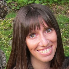 Woman with dark hair smiles while siting outside